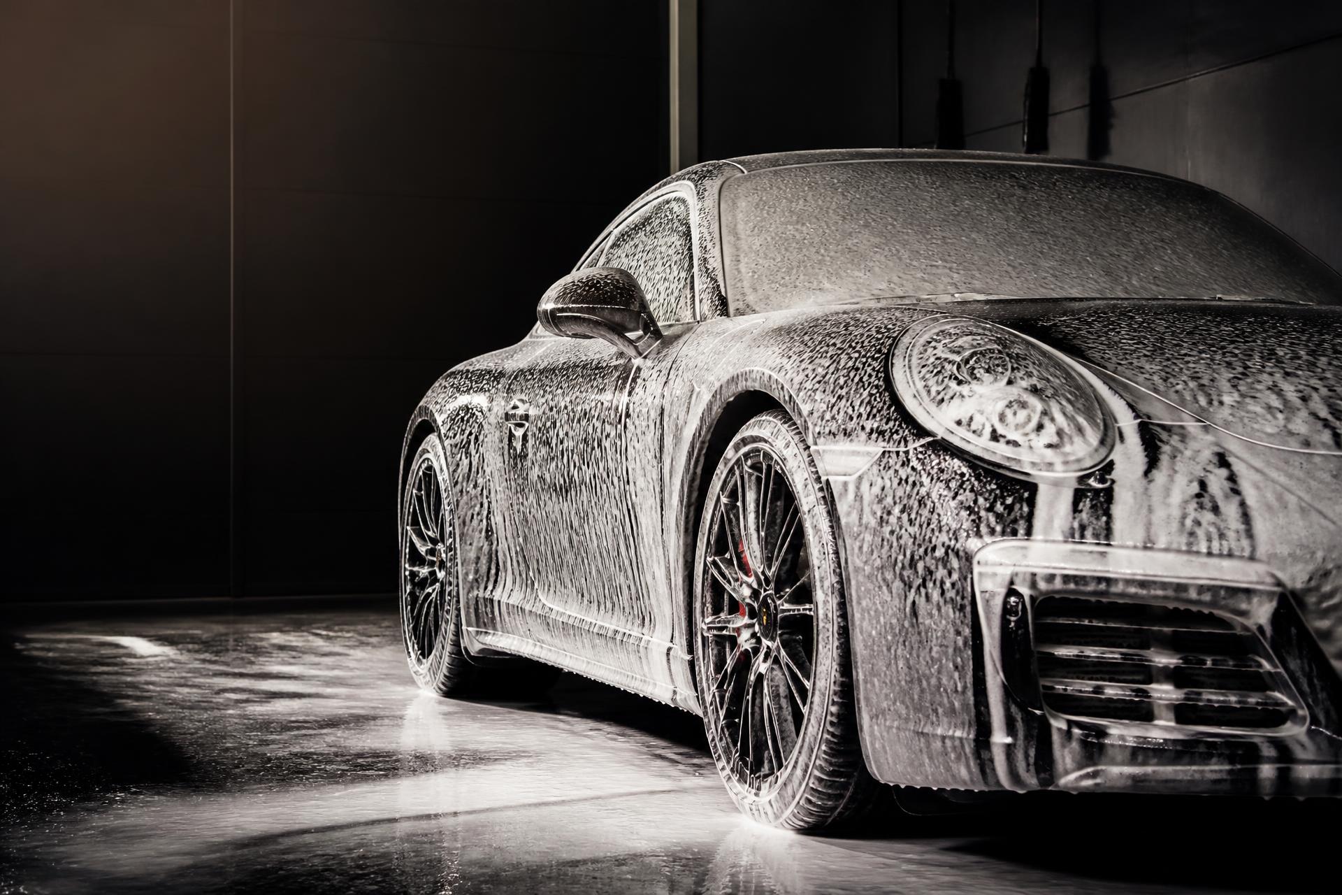 Black sports car covered in snow foam inside a detailing studio